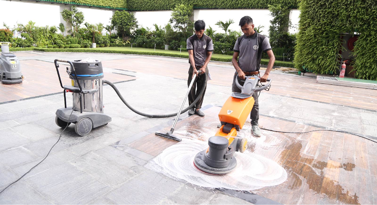 Two HANSA cleaning staff polishing a stone terrace floor with a scrubbing machine and wet vacuum